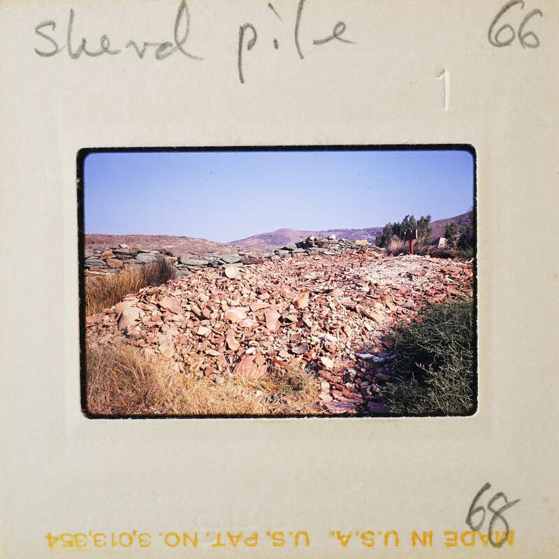 A pile of rocks on a hillside with mountains in the background.