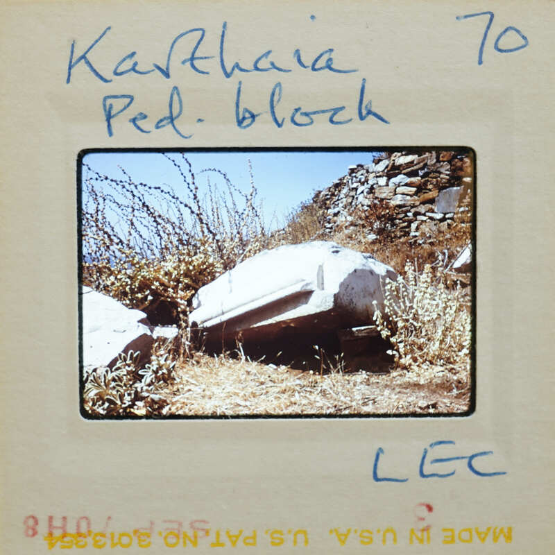 Old stone statue with vegetation growing around it, on a rocky hillside.