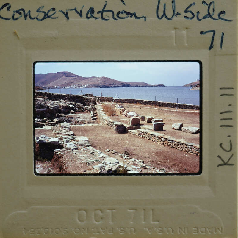 The image is a photograph of an ancient archaeological site with stone ruins overlooking the sea, captured on film and displayed within its original negative frame.
