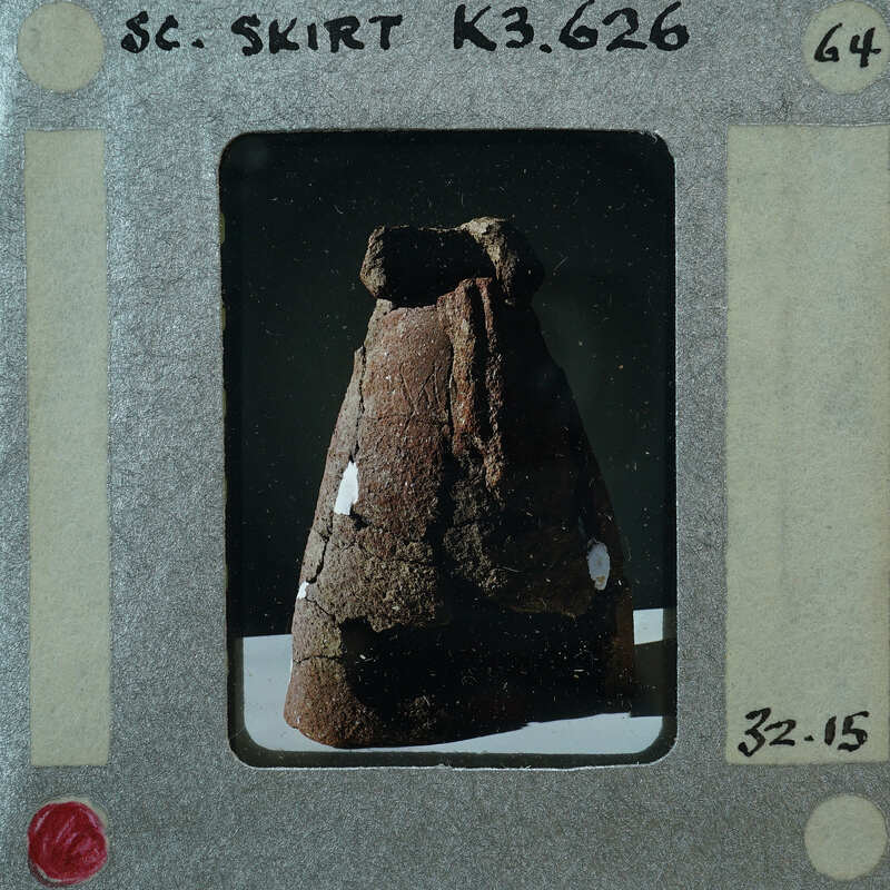 The image shows a vintage Polaroid photo of an artifact, which appears to be a pottery item with a handle and possibly some engravings or markings on its surface. The photograph is placed within the confines of a white Polaroid frame that