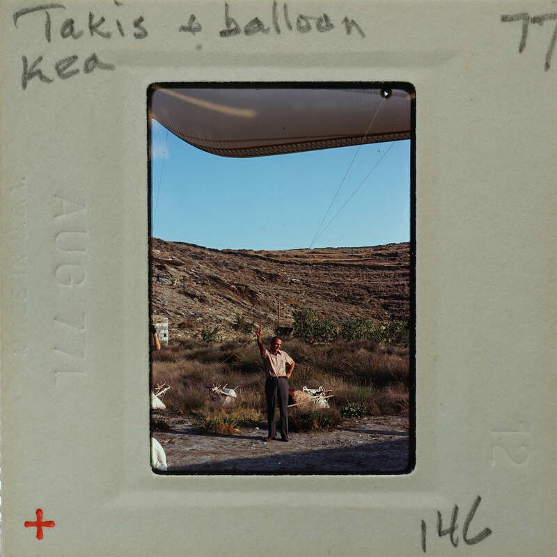Man standing on rocky terrain with a kite flying above him.