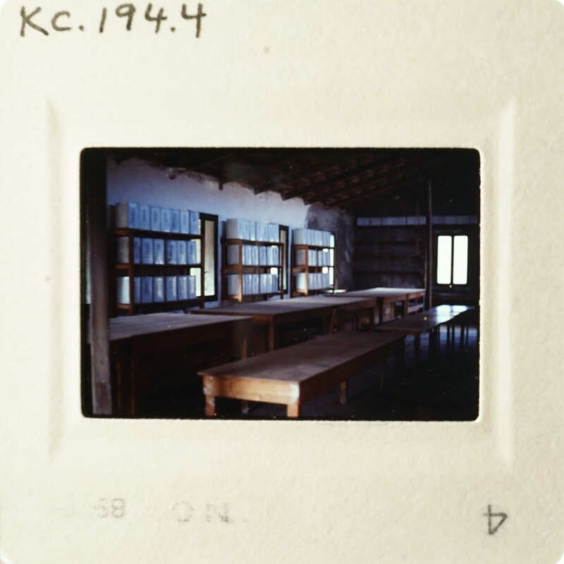 The photo shows an empty library with long tables and rows of bookshelves.