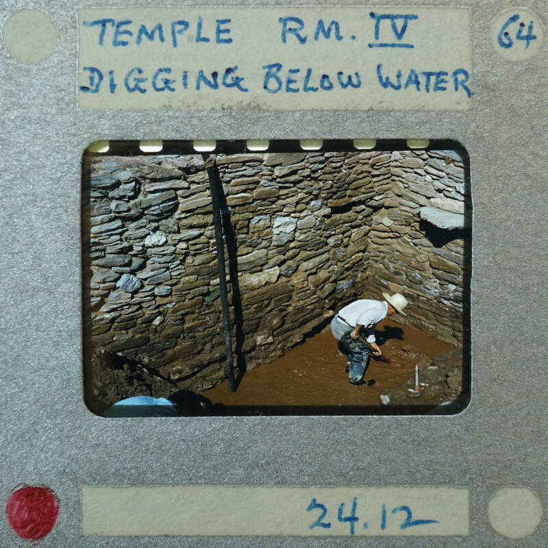 Tall stone wall corner with worker inside digging through mud on the floor.