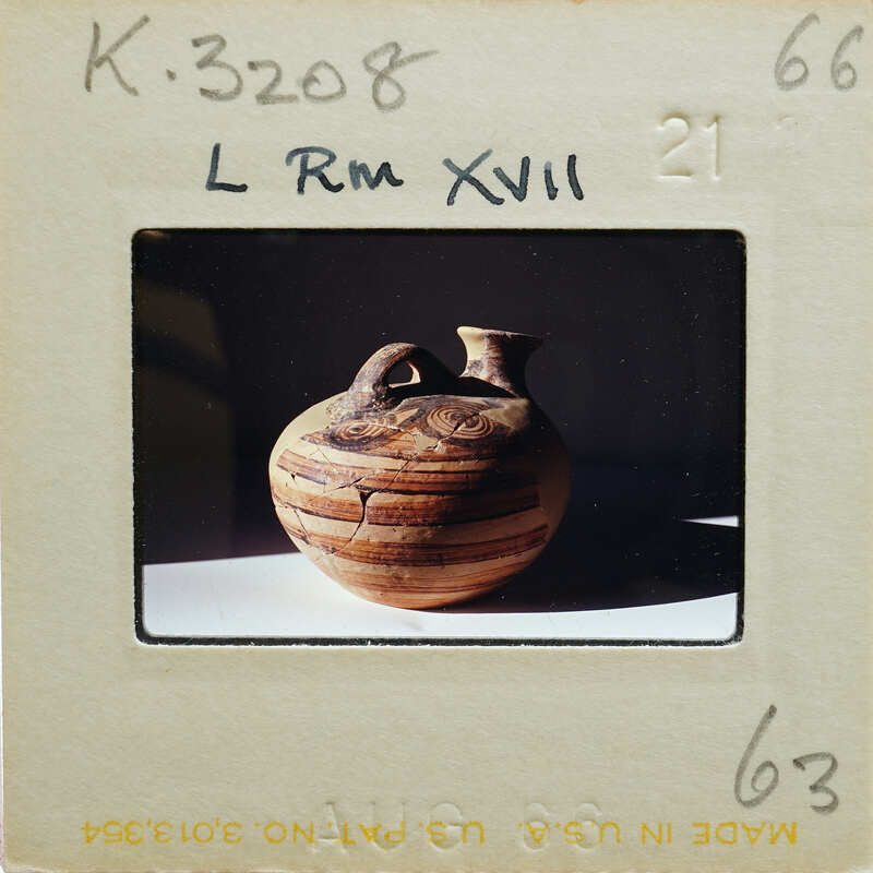Ancient stirrup jar (K.3208) on table with high contrast.