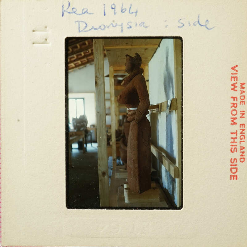 Wooden sculpture on display inside a building with exposed wooden beams and artwork on the wall.