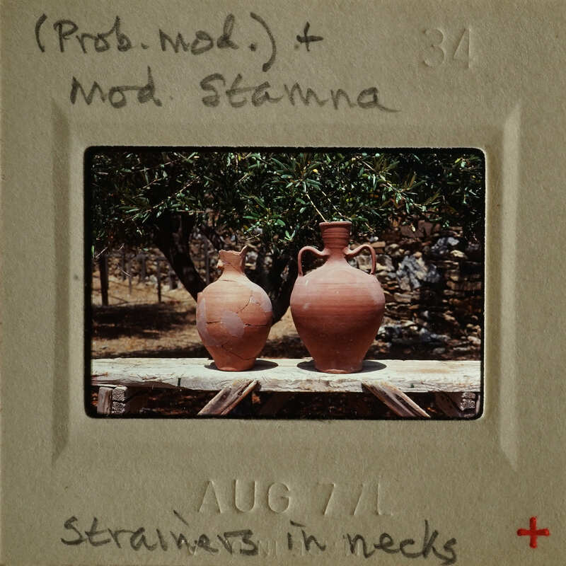 Two clay vases on a wooden surface with greenery in the background.