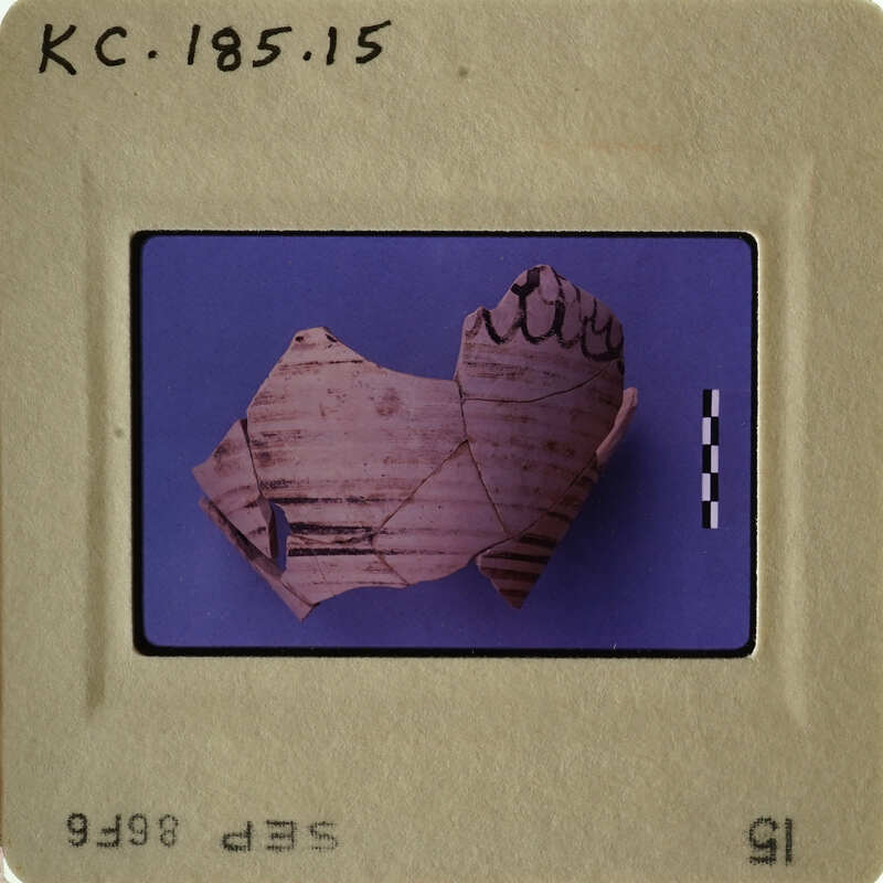 Ancient Greek vase fragment with visible drawing and writing, photographed on a blue background.