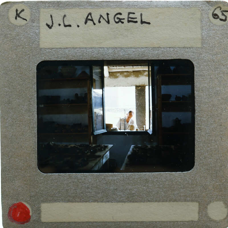 A slide of a person working inside a pottery studio, with shelves filled with clay pots and vases.
