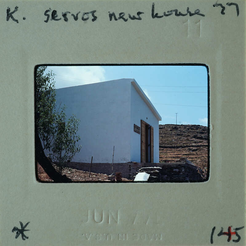 Photo of a small white house with a door and window, surrounded by trees and hills, on a vintage film strip.