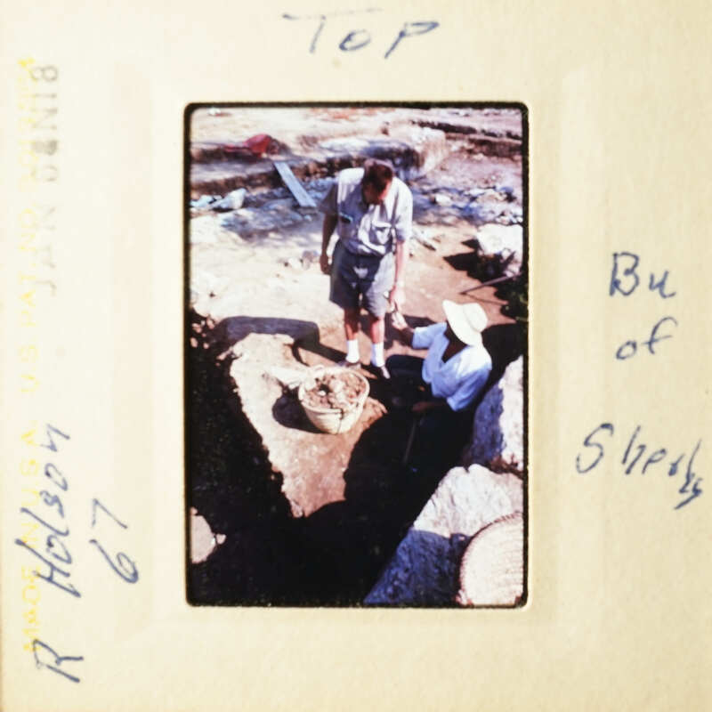 Two people standing by a large hole in the ground, possibly working on an archaeological site.