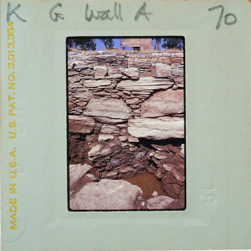 A photograph of a stone structure, possibly ruins or an old building, with visible decay and vegetation growth.