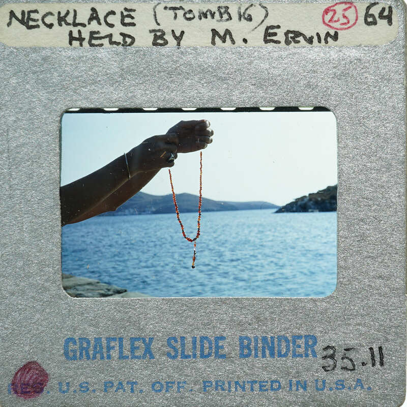 A person holding a necklace over water, with mountains in the background.