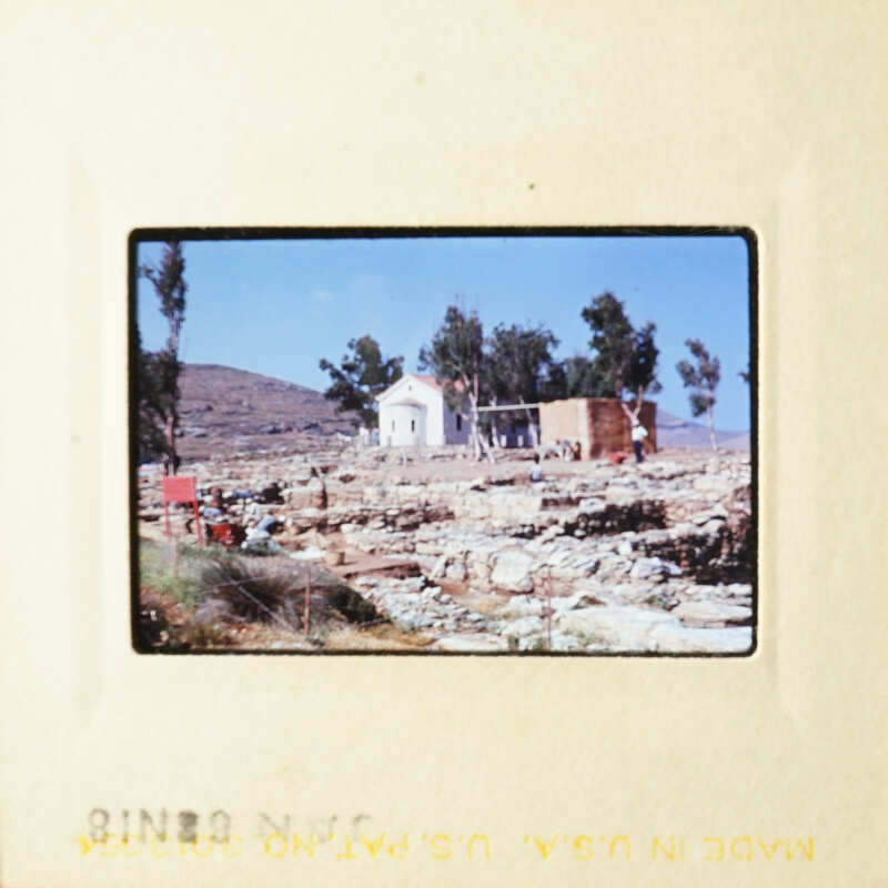 A vintage photograph depicting a small village with a church and stone houses, set against a clear sky.