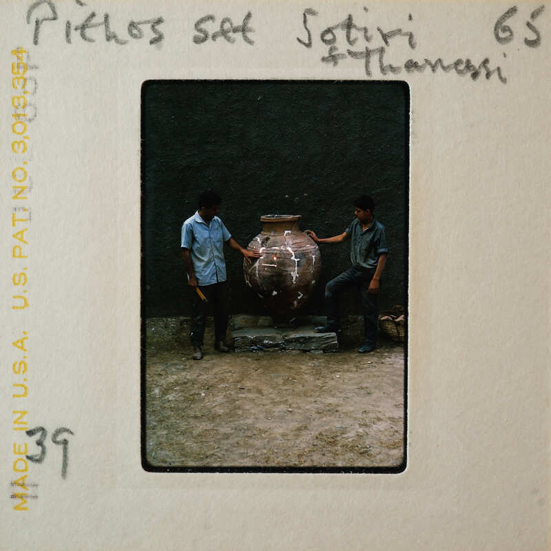Two men standing next to a large clay pot.