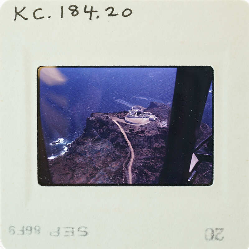 Aerial photograph of a coastal landscape with a road and buildings, taken from a helicopter window.