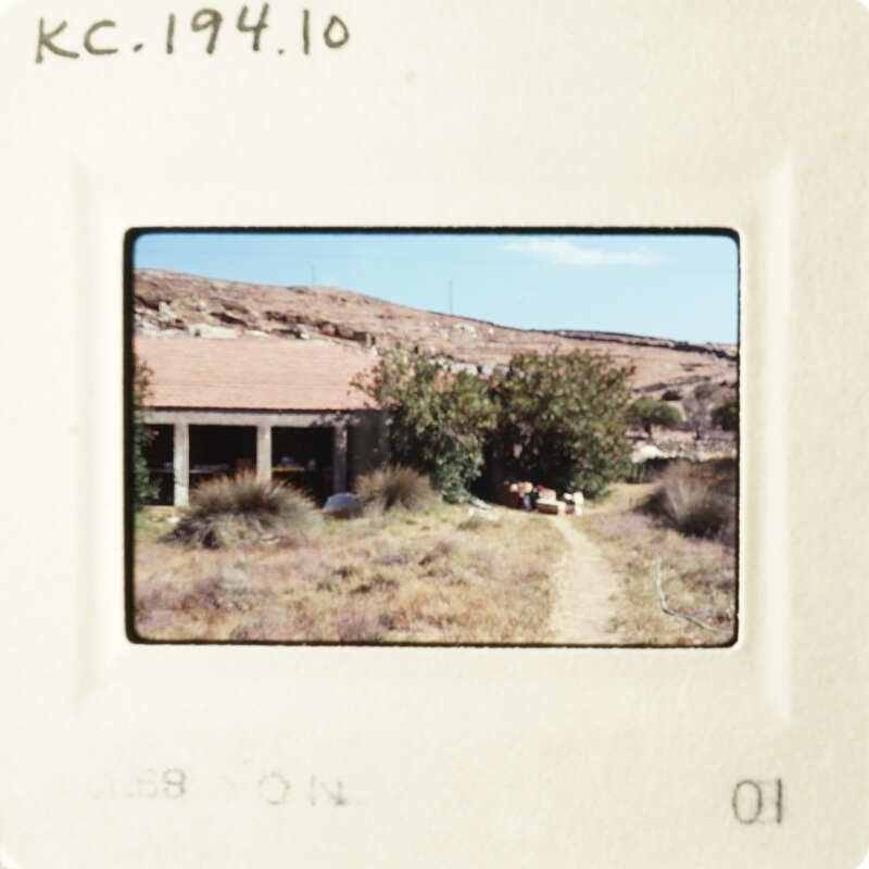 A photograph depicting a rural landscape with a house, trees, and a dirt road.