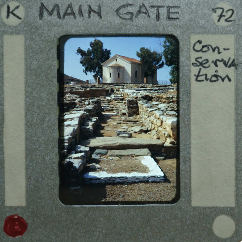 A photograph of an ancient stone pathway with a building and trees in the background, presented as if it's a film strip frame.
