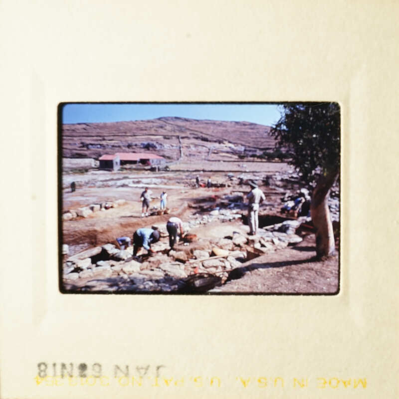 A group of people working on an archeological site, surrounded by stone ruins and dirt.