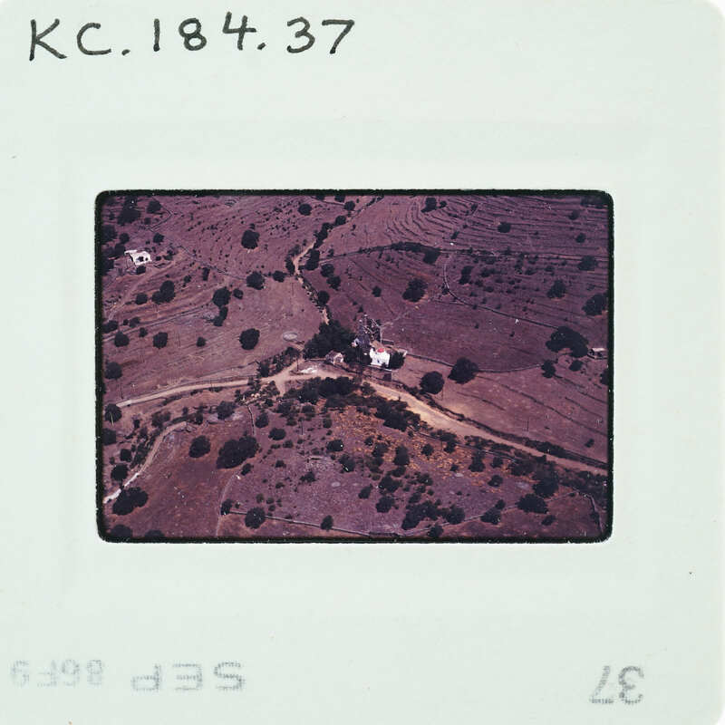 Aerial photograph of a rural landscape with dirt roads and sparse vegetation, enclosed by a white border with handwritten notes.