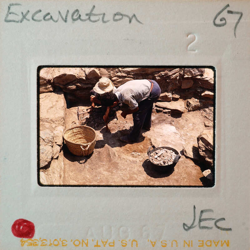 Two people working on an archaeological excavation site with stone ruins and tools.