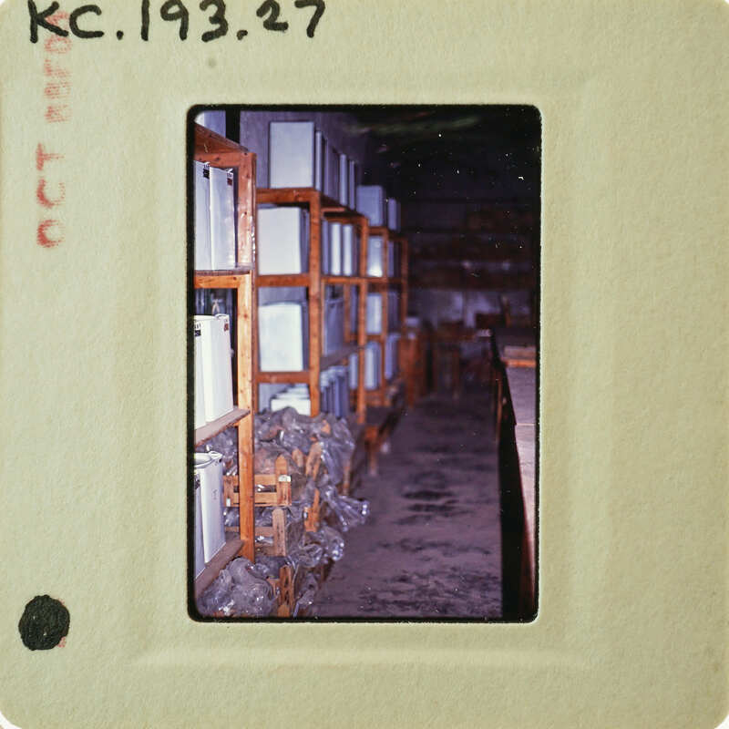 A photograph of a room filled with wooden shelves and boxes, taken from an angle that shows the perspective of looking into the space.