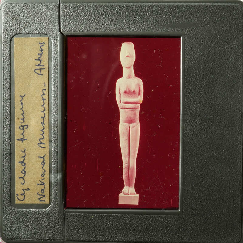 Ancient Egyptian artifact, possibly a figurine or amulet, displayed on a red background with labels and markings.