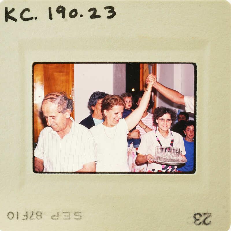 A vintage photo of a man and woman celebrating with cake, surrounded by friends. Catalog number KC.190.23