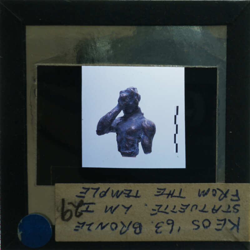 A photograph of a sculpture with its hand raised to the face, displayed on a card with printed information and an arrow pointing right.
