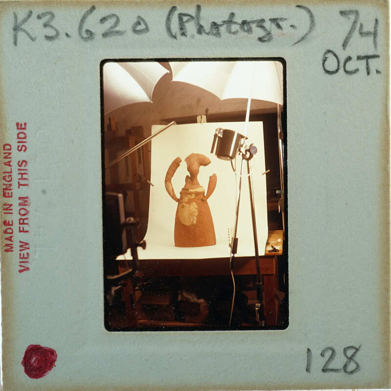 Terracotta figurine partially restored on table with photograph lamps set up.