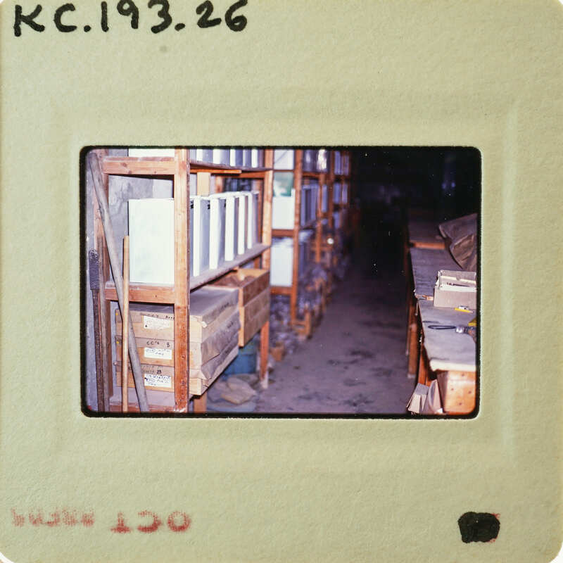 Old photo of a library with shelves filled with books and papers, taken from an angle that shows the interior space.
