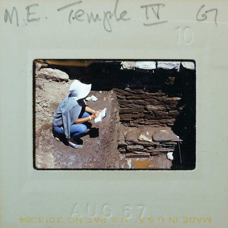 Person working on archaeological site, examining ancient ruins.