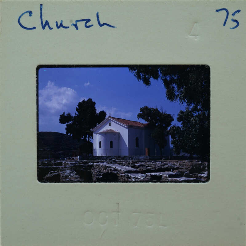 A vintage photograph of an old church with a stone facade and trees around it, placed within a film strip holder.