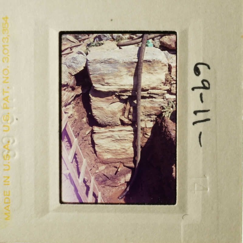 This is an image of a stone wall with a wooden pole leaning against it, taken from a low angle, and placed in a film strip frame.