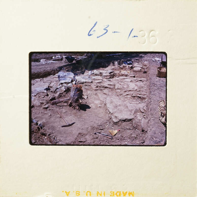 A photograph of an archaeological site with exposed stone ruins and excavation tools.