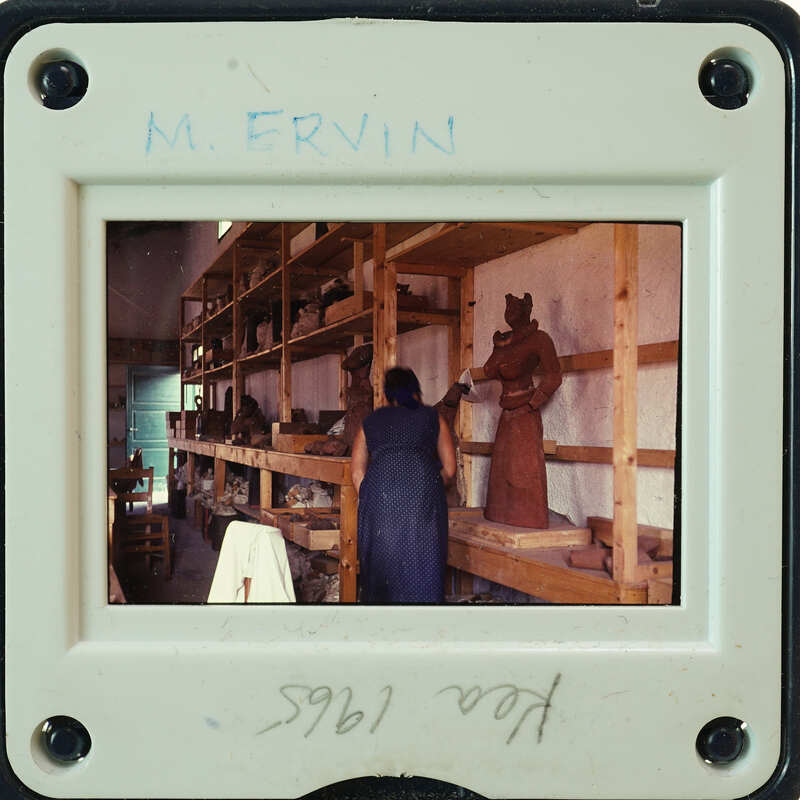 A photograph of a person working on pottery, surrounded by shelves filled with various ceramic items.