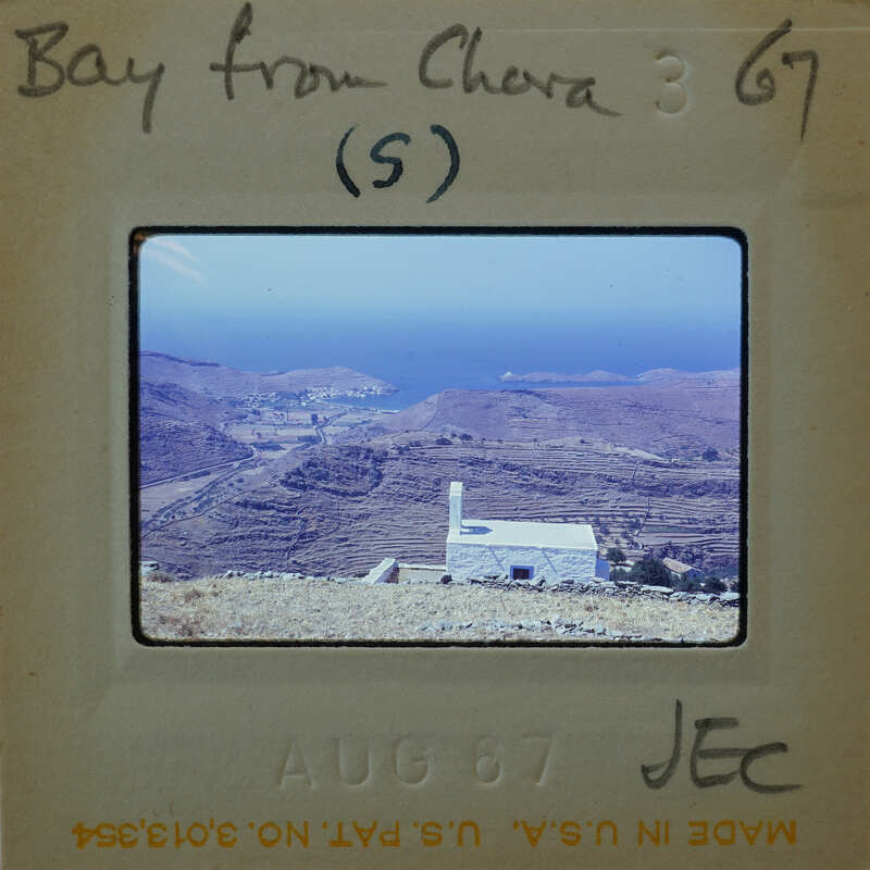 Slide of a coastal landscape with mountains, water, and a small white building.