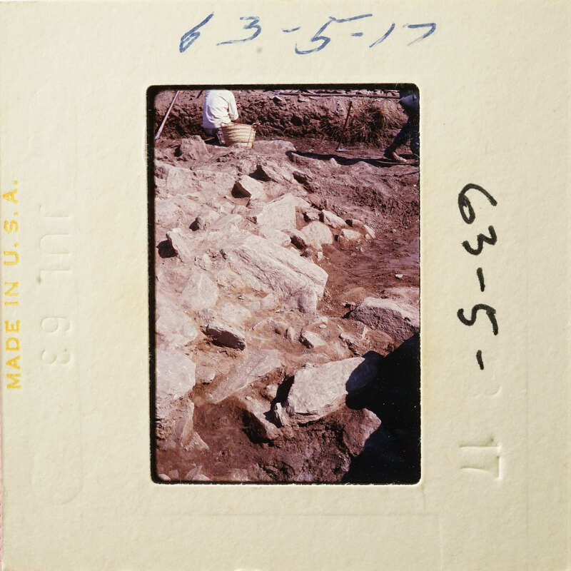 Old photograph of an archaeological site with excavated stone ruins and people working on-site.