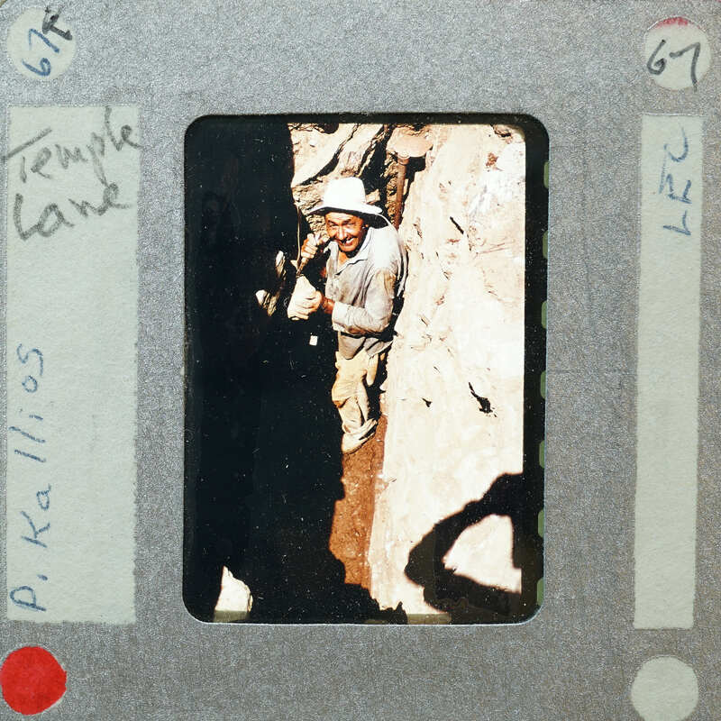 A vintage photograph of a man with a hat, standing near rocks and dirt, possibly during an archaeological or exploration activity.