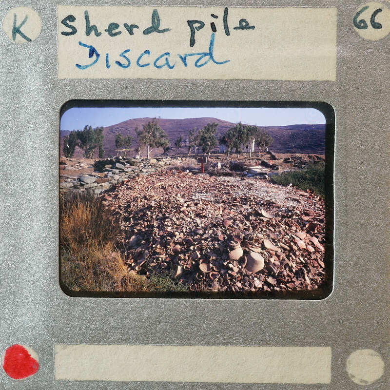 A pile of discarded items, possibly from a demolition site or construction waste, with mountains and trees in the background.