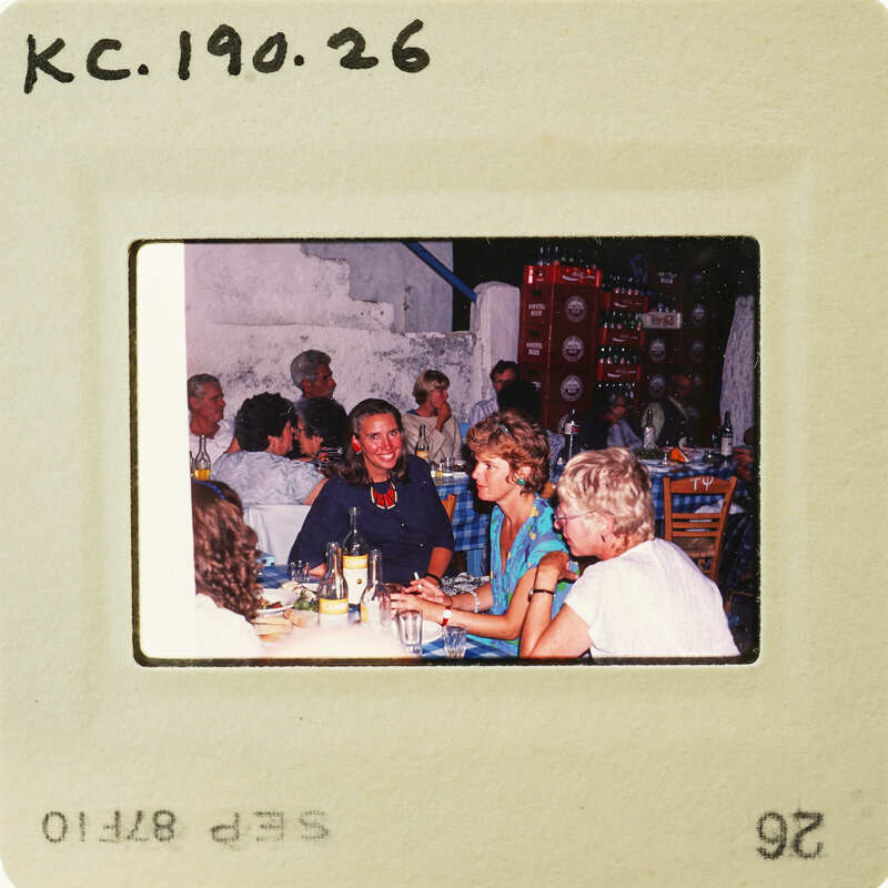 A vintage photo of a group of people sitting around a table, possibly at a social gathering or event. Catalog number KC.190.26