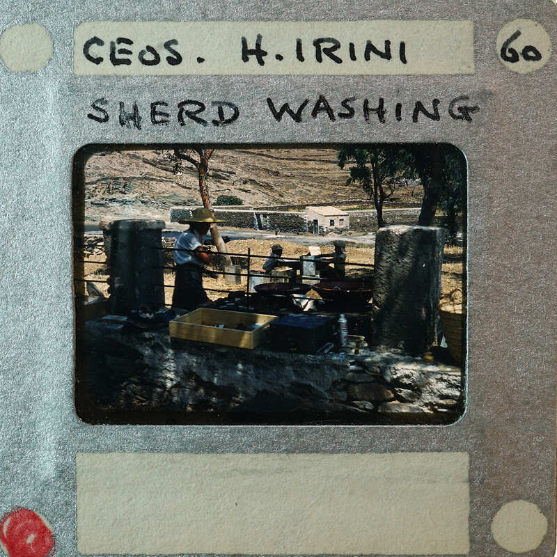 A vintage photo of a woman washing clothes by a river, with an old-fashioned appearance and handwritten label.