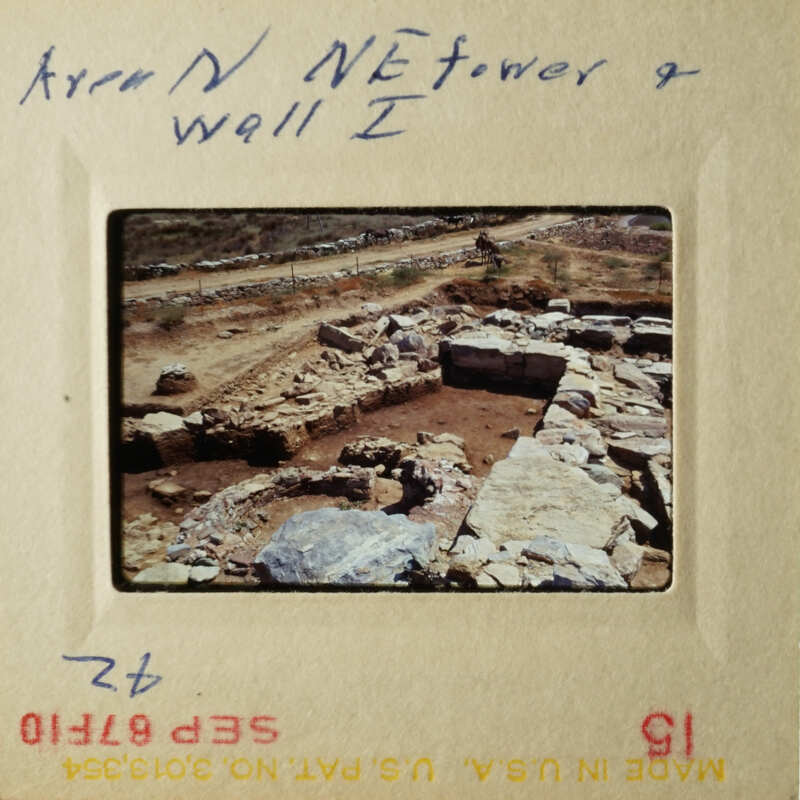 This is a photograph of an archaeological site with stone ruins and a dirt road, taken from a high angle perspective.