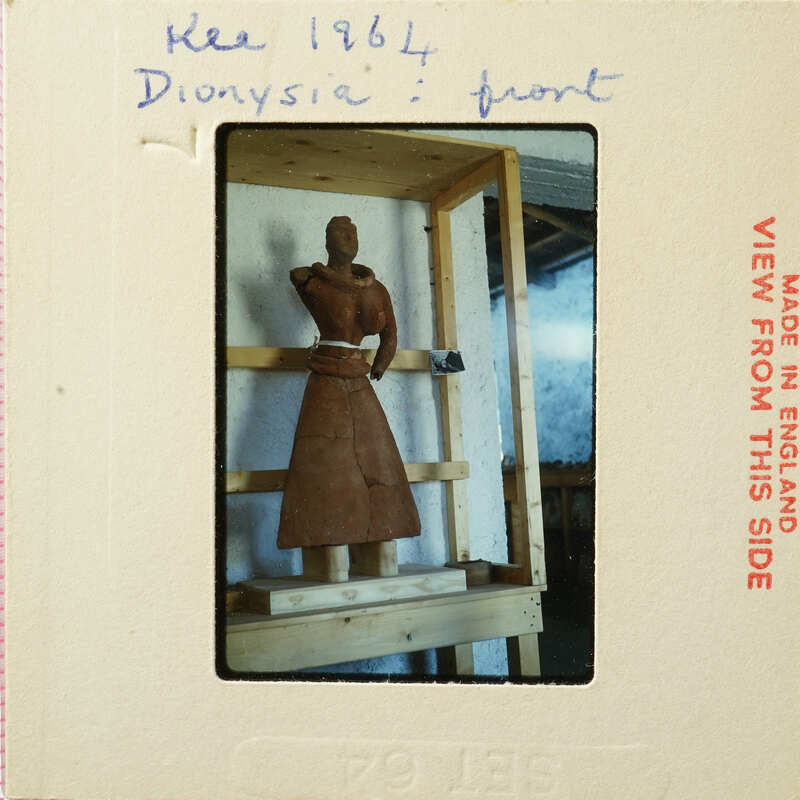 A sculpture of a person wearing a dress, displayed on a wooden stand.