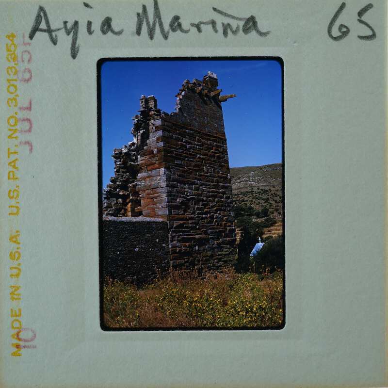 Old stone ruins on a hillside with blue sky and greenery.