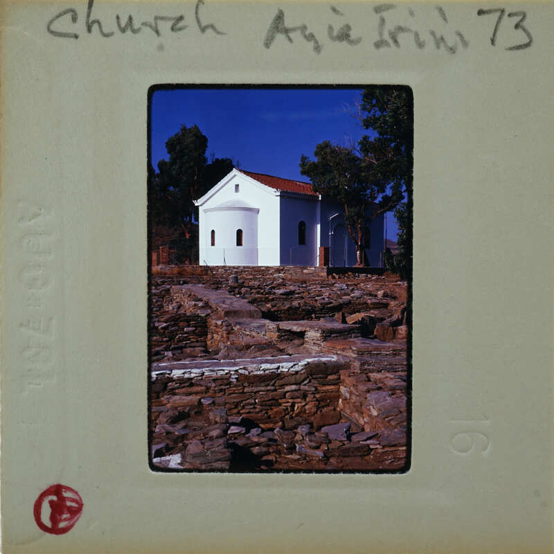 A vintage photograph of a white church with a stone path leading to it, set against a blue sky and trees.