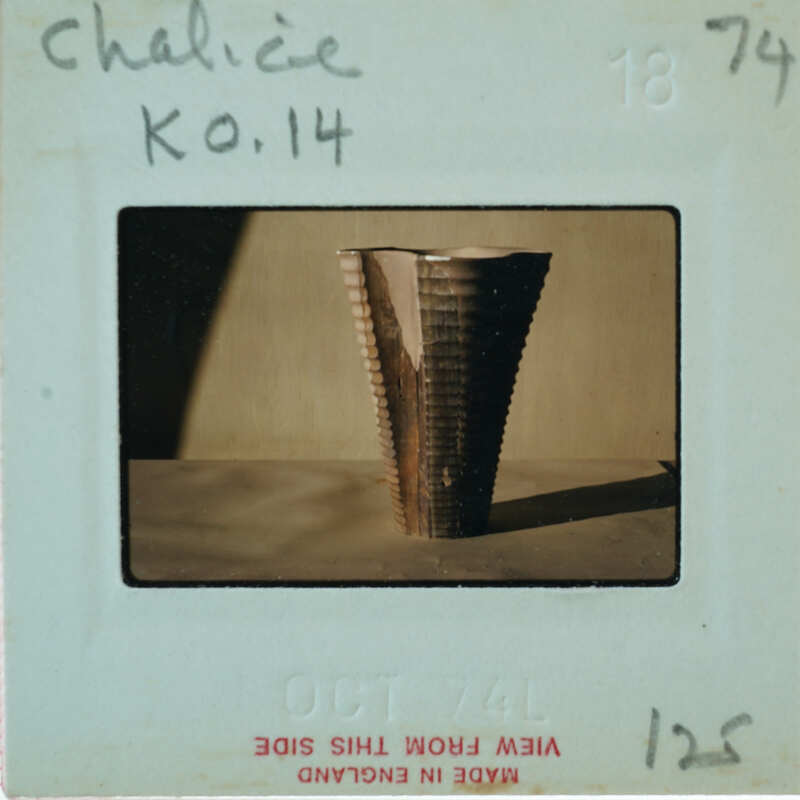 A photograph of a tall, narrow vase with ridges on its surface.