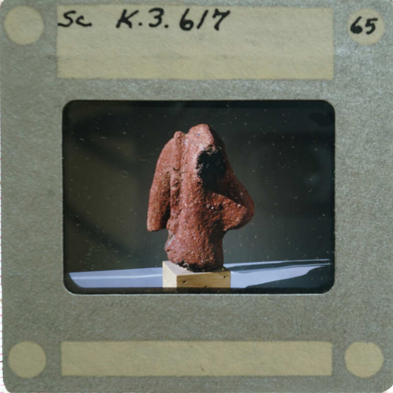 A photograph of a clay figurine torso, displayed on a stand.