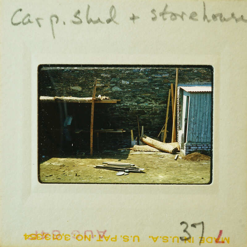 Old photograph of a dilapidated shed and storehouse with wooden structure, stone walls, and metal roof.