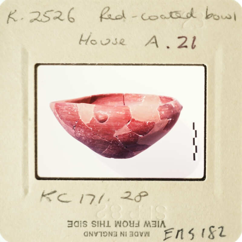 A photograph of an antique red clay bowl with visible cracks and imperfections, displayed on a card labeled "House A" with handwritten notes.