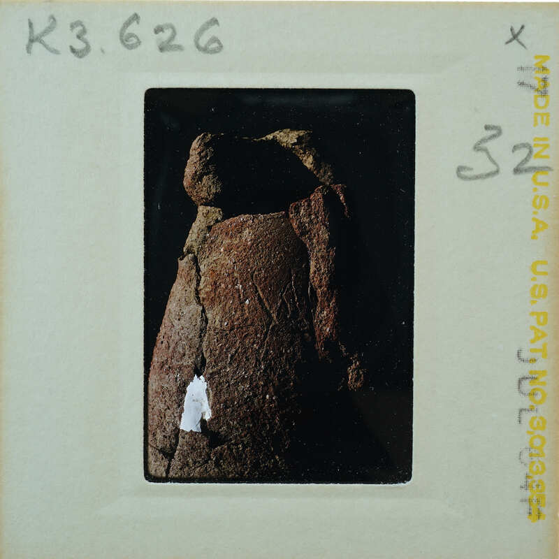 A black and white photograph of a weathered, possibly ancient stone sculpture with markings.